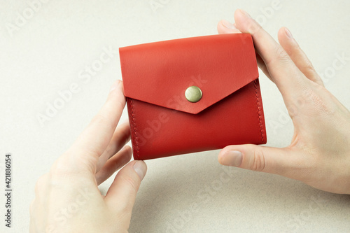red leather wallet in female hands close-up on a gray background
