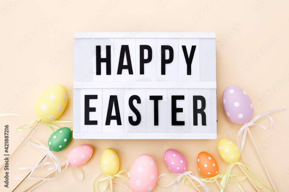 Easter greeting on lightbox with colorful eggs on sticks. Top view on a beige background