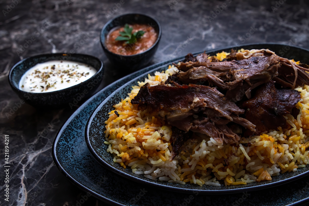 A plate of kabsa rice and grilled lamb and two small plates of Yogurt and hot sauce. A plate of kabsa rice and grilled lamb and two small plates of Yogurt and hot sauce.