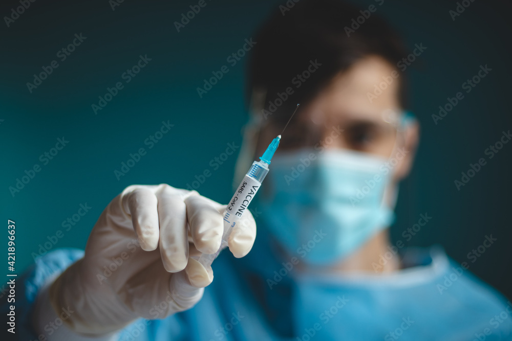 doctor in a sterile protective suit with a shield on his head prepares a syringe with a Covid-19 vaccine for an incoming patient. Medical worker. Fighting a pandemic. Blue tone doctor in a sterile protective suit with a shield on his head prepares a syringe with a Covid-19 vaccine for an incoming patient. Medical worker. Fighting a pandemic. Blue tone