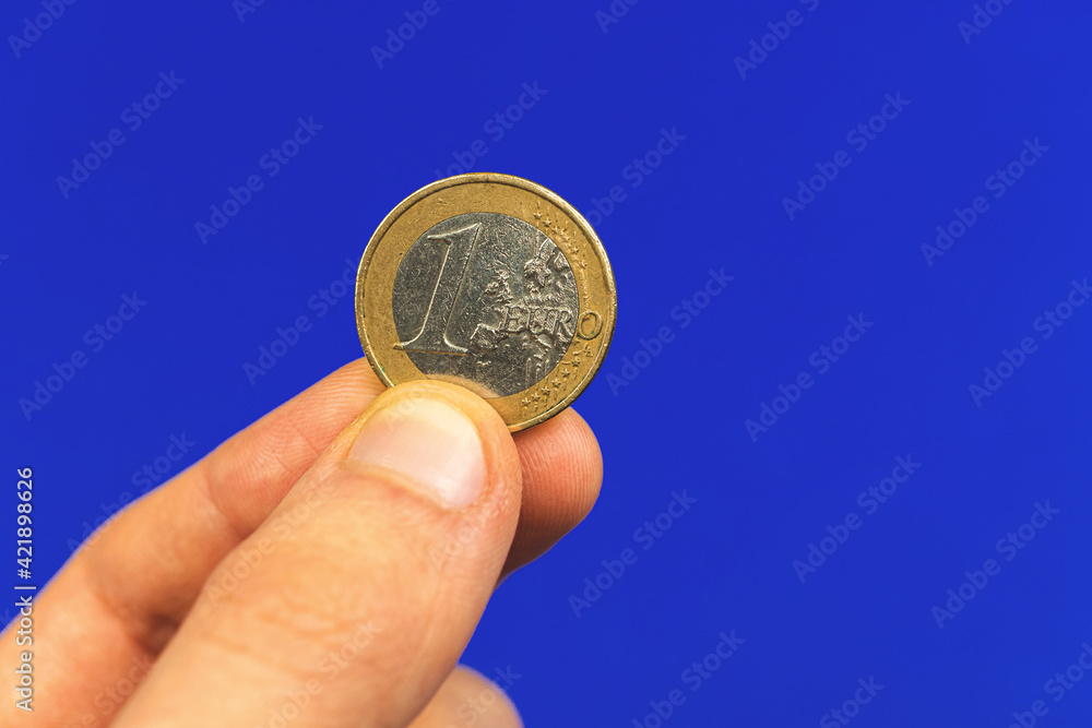 Hand hold one euro coin on a blue isolated background, close-up Hand hold one euro coin on a blue isolated background, close-up