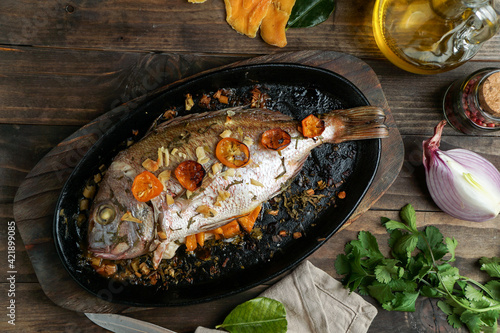 baked or roasted porgy in the black cast iron brazier with oil and cilantro and spices photo