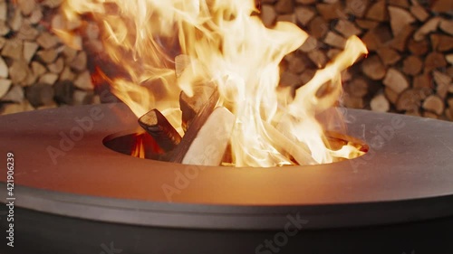 The young woman and her boyfriend are throwing firewood into a round metal designer brazier and light a fire.