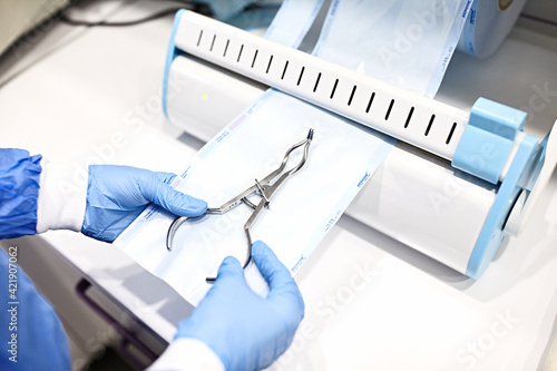 Sterilizing medical instruments in autoclave. Dental office. Close up dentist assistant's hands holding packaged with vacuum packing machine medical instruments ready for sterilizing in autoclave.