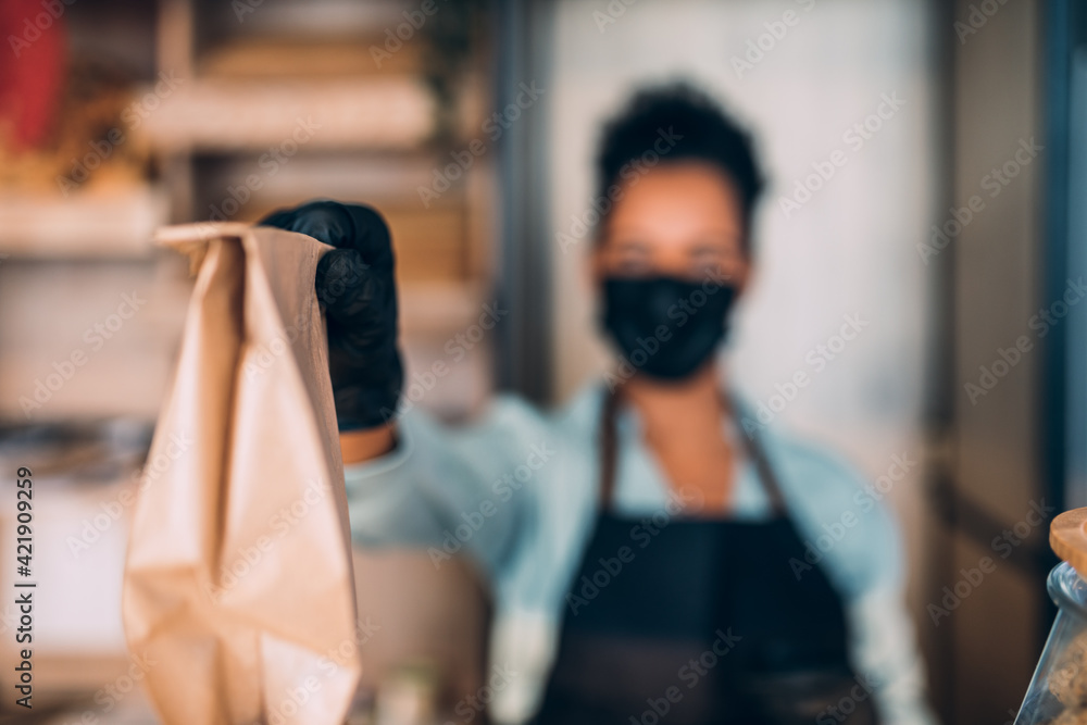 African American middle aged female worker with protective mask on face working in bakery. Coronavirus, Covid-19 concept.