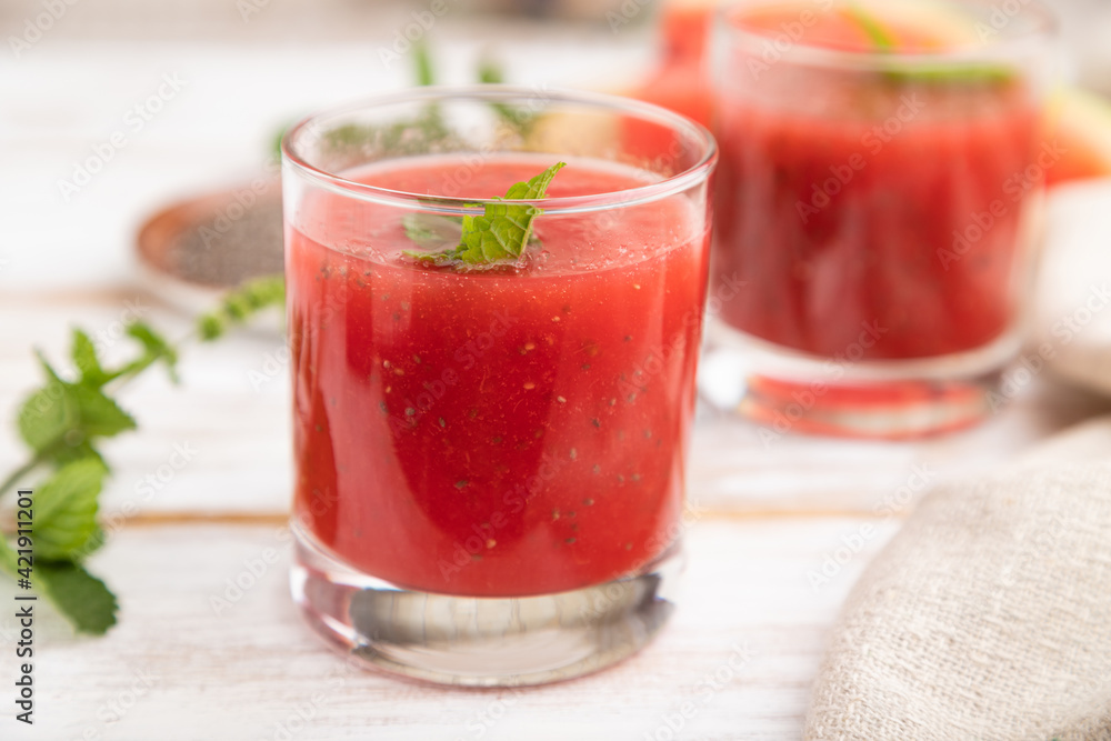 Watermelon juice with chia seeds and mint in glass on a white wooden background with linen textile. Side view, selective focus. Watermelon juice with chia seeds and mint in glass on a white wooden background with linen textile. Side view, selective focus.