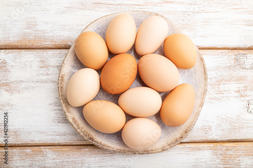 Pile of colored eggs on plate on a white wooden background. top view, close up.