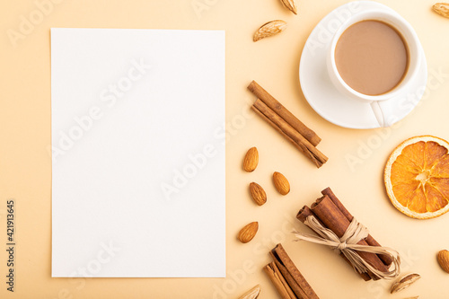 Composition with white paper sheet, almonds, cinnamon and cup of coffee. mockup on orange background. top view, copy space.