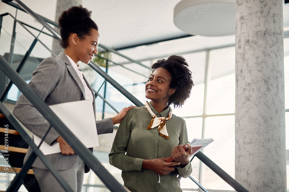 Happy black businesswoman talks to female mentor who leads her through office building. - obrazy, fototapety, plakaty 
