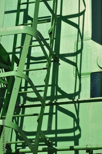 Green painted metal ladder of construction crane with geometric shadows. Industrial heavy machinery stairs. Construction and transportation equipment