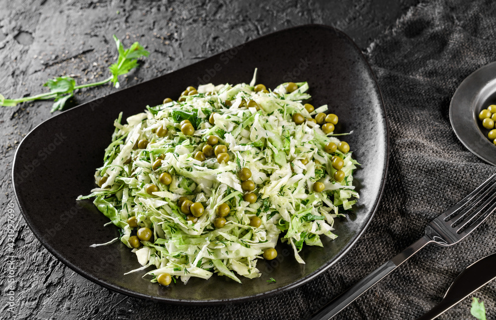 Fresh salad with cabbage, herbs and green peas served on a plate over a dark background, close up. Concept of healthy food, clean eating Fresh salad with cabbage, herbs and green peas served on a plate over a dark background, close up. Concept of healthy food, clean eating