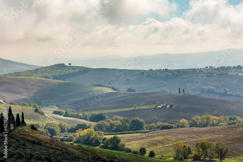 Sunny day landscape rural view, Tuscany, Italy. Misty dramatic cloudy autumn sky, layered green hills