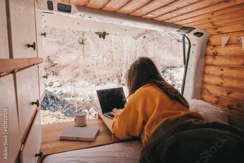 Vanlife - Young woman working on notebook in camping van surrounded by nature