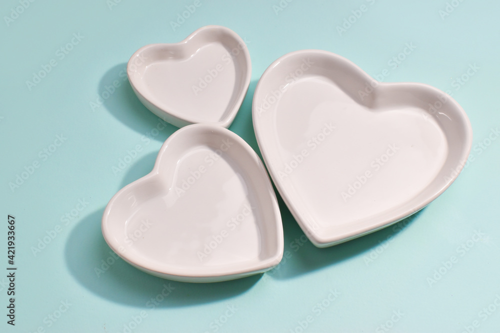 Three ceramic plates in the shape of a heart on a blue background, top view. Tableware. Three ceramic plates in the shape of a heart on a blue background, top view. Tableware.