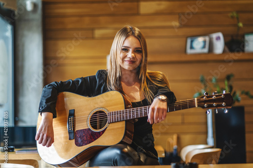 Front view portrait of adult caucasian woman sitting at empty cafe with guitar on her lap looking to the camera - female musician relaxed real people leisure concept photo