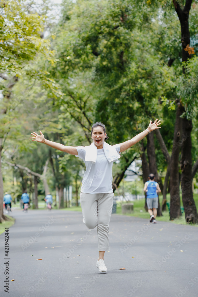 asian woman senior sportswear cheerful running and arms outstretched. joyful exercise in garden. happy mature healthy lifestyle.