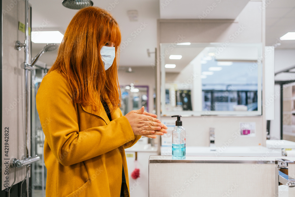 Young woman wearing a face mask applying hand sanitizer in the shop Young woman wearing a face mask applying hand sanitizer in the shop
