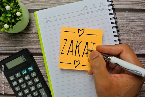 Calculator, flower, sticky note and hand write word ZAKAT. Zakat is muslim tax to help each other.