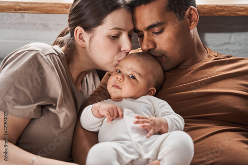 Multiracial family embracing their cute little child and kissing him