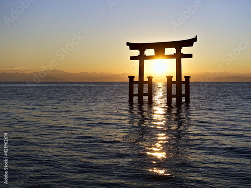 the sun rises from behind the lake between the shutters of the Shinto torii gates, standing in the water