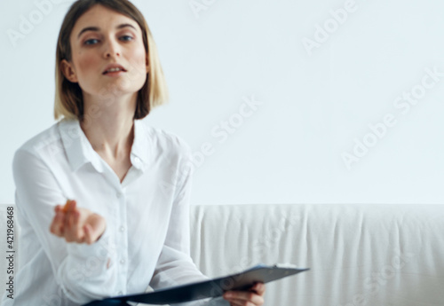 a woman in a shirt with documents in her hands sits on a sofa indoors