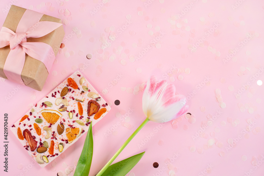 View of gift box, flower and Handmade pink chocolate bar with dried fruits and nuts on a fastive Pink Background View of gift box, flower and Handmade pink chocolate bar with dried fruits and nuts on a fastive Pink Background