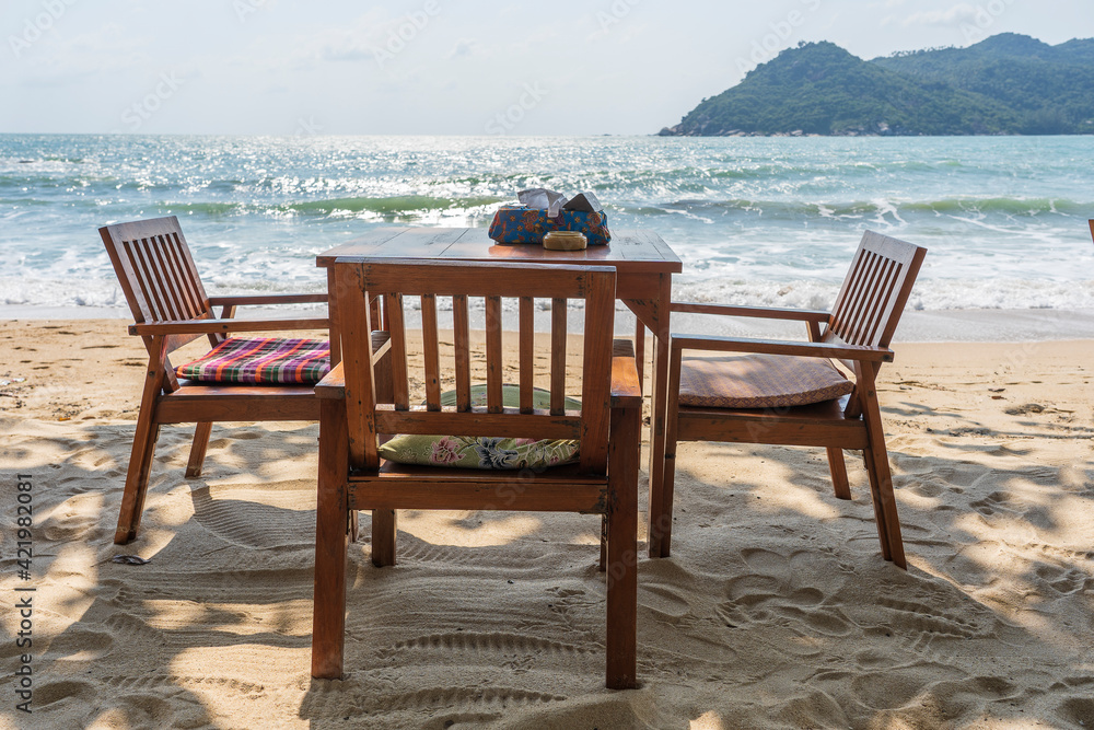 Wooden table and chairs in empty beach cafe next to sea water. Close up, Thailand