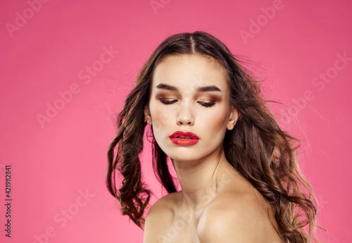 Sexy brunette with loose hair on a pink background with bright makeup