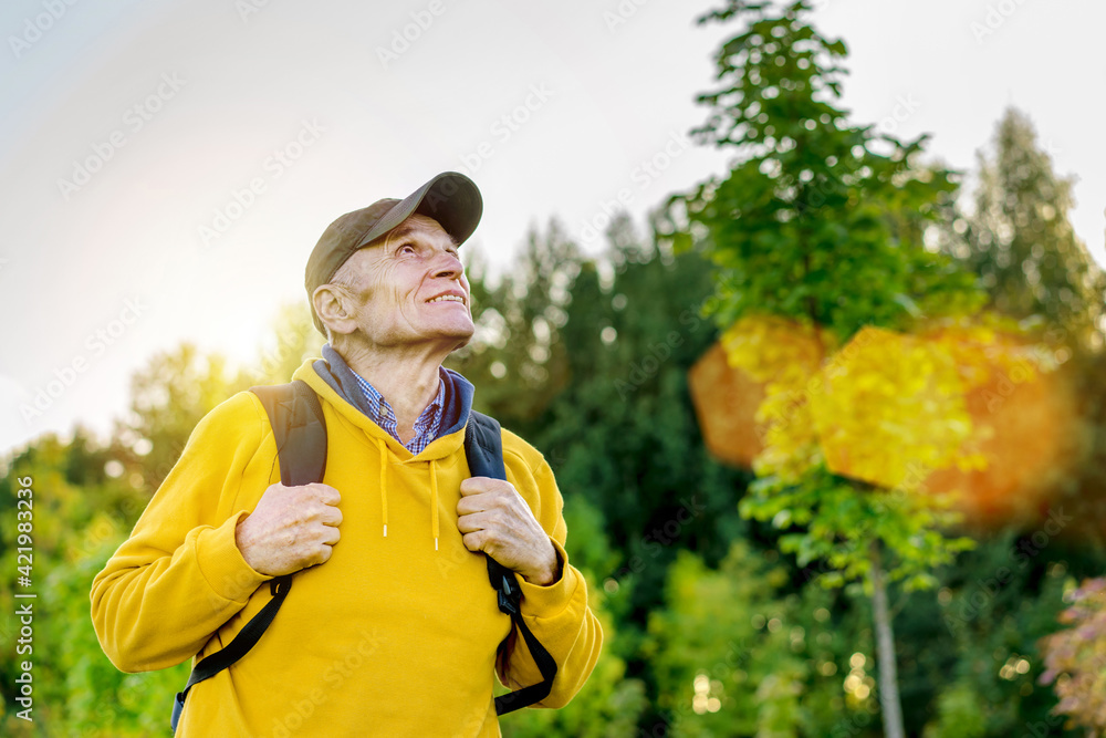 Naklejka premium Senior hiker in cap and with rucksack looks in mountain top.