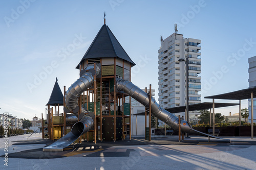 Fotografie Parque infantil con juegos y tobogán, ciudad de fondo