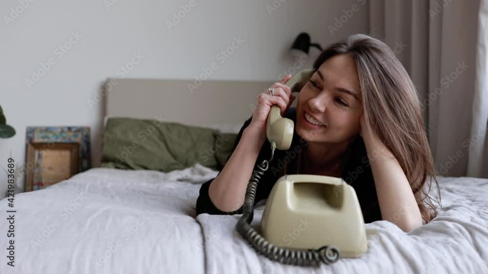 Young business woman with long hair on the bed talking on an old worn out landline phone. Young business woman with long hair on the bed talking on an old worn out landline phone.