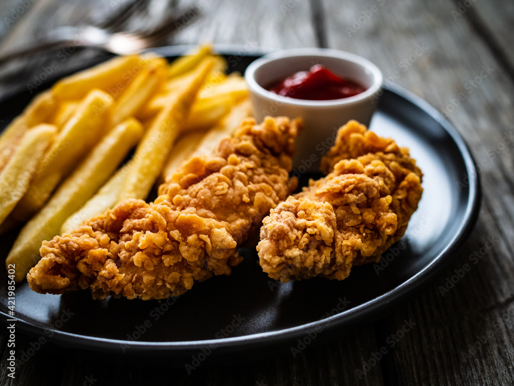 Fried breaded chicken nuggets with French fries and ketchup on wooden table
Fried breaded chicken nuggets with French fries and ketchup on wooden table
