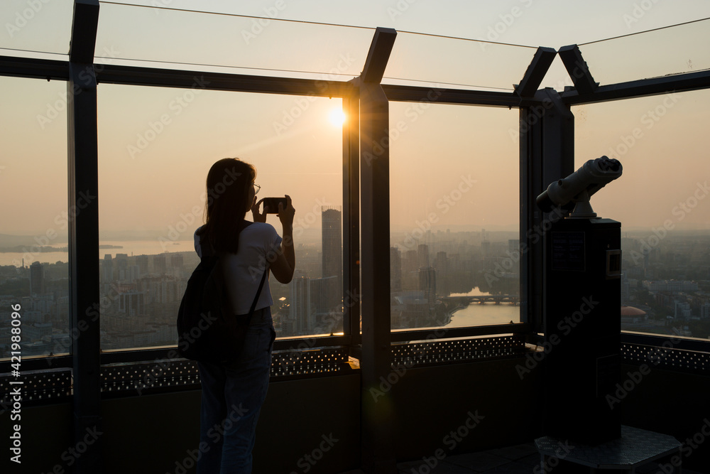 Fototapeta premium the silhouette of a girl standing on the observation deck and looking at the sunset