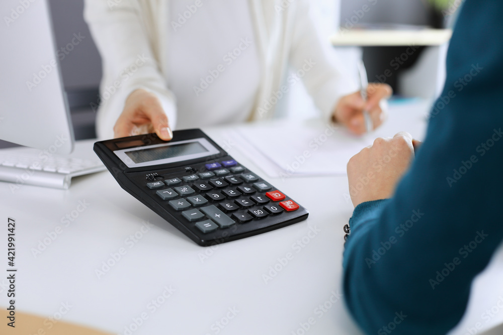 Accountant checking financial statement or counting by calculator income for tax form, hands close-up. Business woman sitting and working with colleague at the desk in office. Audit concept Accountant checking financial statement or counting by calculator income for tax form, hands close-up. Business woman sitting and working with colleague at the desk in office. Audit concept