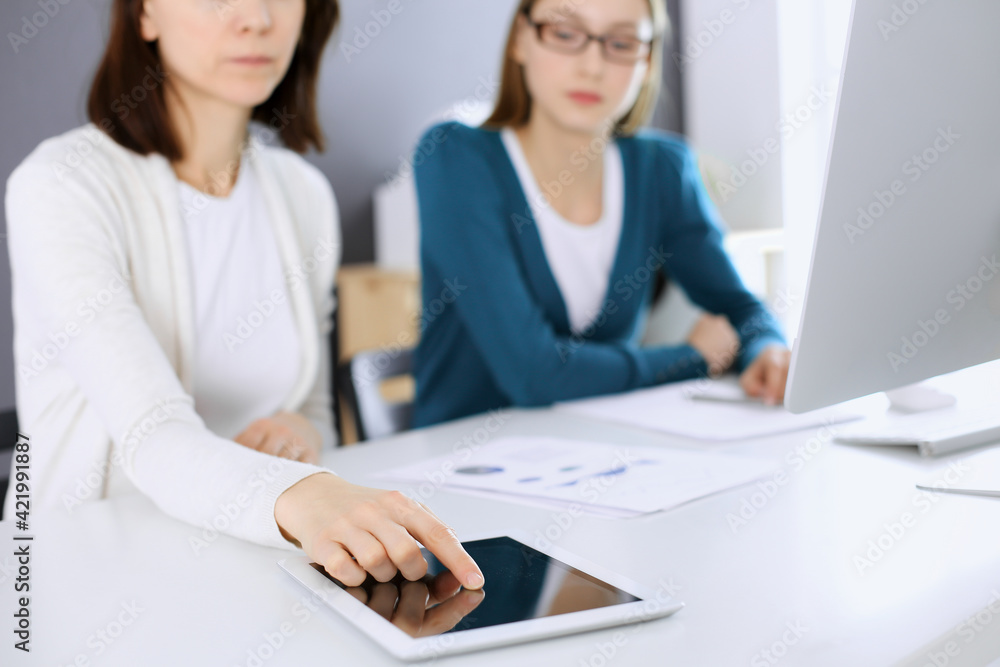 Businesswoman pointing at tablet computer screen while giving presentation to her female colleague. Group of business people working at the desk in office. Teamwork concept Businesswoman pointing at tablet computer screen while giving presentation to her female colleague. Group of business people working at the desk in office. Teamwork concept