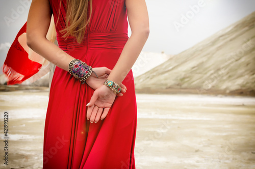 A woman in a red dress holds her hands from behind. The woman is wearing beautiful bracelets.