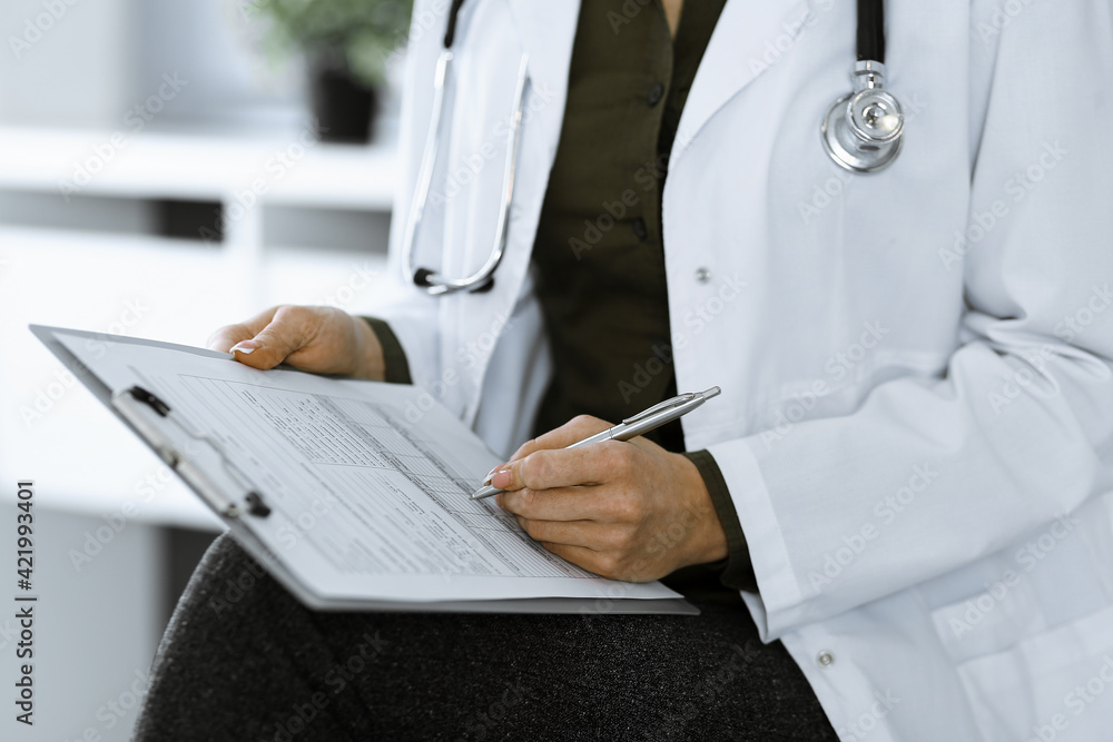 Unknown woman-doctor writing something at clipboard while sitting at the chair, close-up. Therapist wearing green blouse at work is filling up medication history record. Medicine concept Unknown woman-doctor writing something at clipboard while sitting at the chair, close-up. Therapist wearing green blouse at work is filling up medication history record. Medicine concept