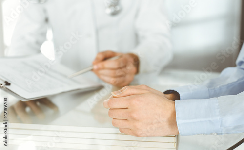 Unknown male doctor and woman-patient discussing current health examination while sitting in clinic and using clipboard. Good medical service in hospital. Medicine concept