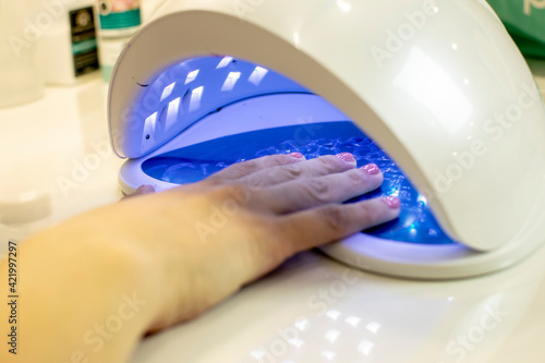 Drying of the varnish applied to the nails in a professional ultraviolet machine.