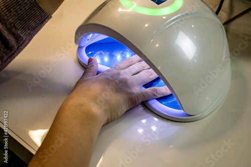 Drying of the varnish applied to the nails in a professional ultraviolet machine.