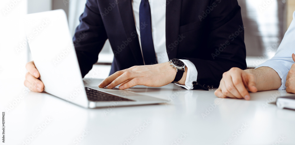 Unknown business people using laptop computer at the desk in modern office. Businessman or male entrepreneur is working with his colleague. Teamwork and partnership concept Unknown business people using laptop computer at the desk in modern office. Businessman or male entrepreneur is working with his colleague. Teamwork and partnership concept