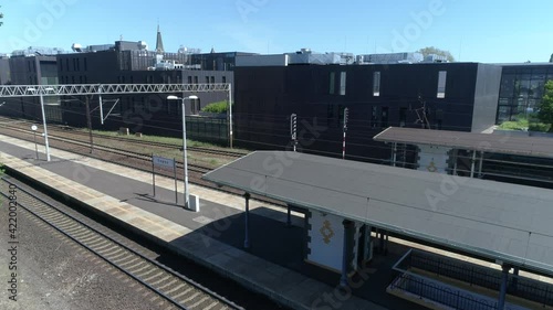 An atmospheric railway station in Sopot, Poland with platforms and a departing long-distance train. In the further part of the drone view, the city, old buildings and the Baltic Sea are visible.