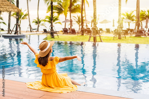 Canvas Print Young woman traveler relaxing and enjoying the sunset by a tropical resort pool