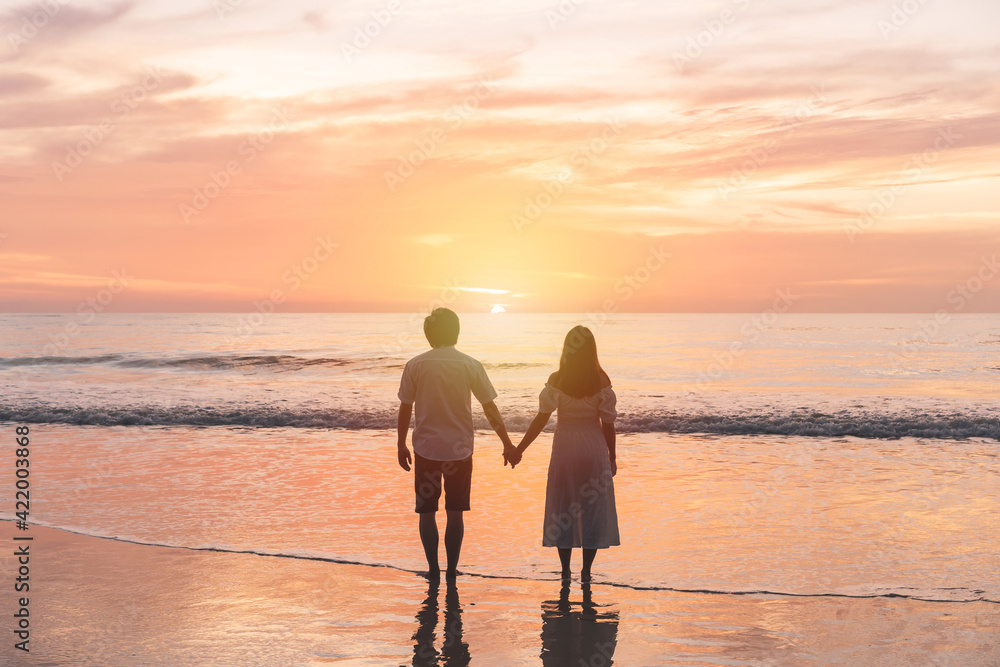 Young Asian couple holding hand together and looking beautiful sunset on the beach, Summer vacation concept
