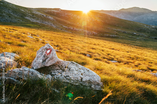 Rising Sun over the Sinjal or Dinara (1831 m) mountain - the highest point of Croatia in the Dinaric Alps on the border between Croatia and Bosnia and Herzegovina. Hiking trail mark painted on rock. photo