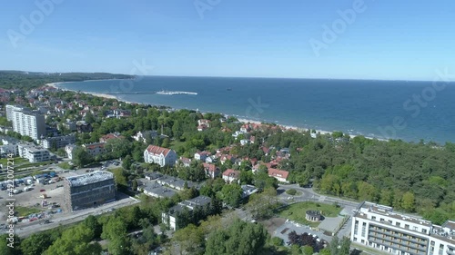 Sopot in Poland on a video from a drone. In the foreground a park with lots of green trees. Few city buildings and in the background the Baltic Sea and the famous Sopot Pier.