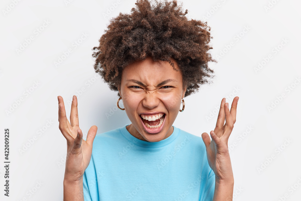 Outraged annoyed young curly African American gestures angrily screams from anger and disappointment shakes hands looses temper yells upset isolated over white background. Negative emotions. Outraged annoyed young curly African American gestures angrily screams from anger and disappointment shakes hands looses temper yells upset isolated over white background. Negative emotions.