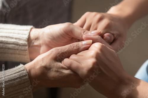 Crop close up of loving elderly mother hold hands of adult daughter show support and care. Supportive mature mom parent comfort caress millennial grownup child. Family unity, bonding concept.