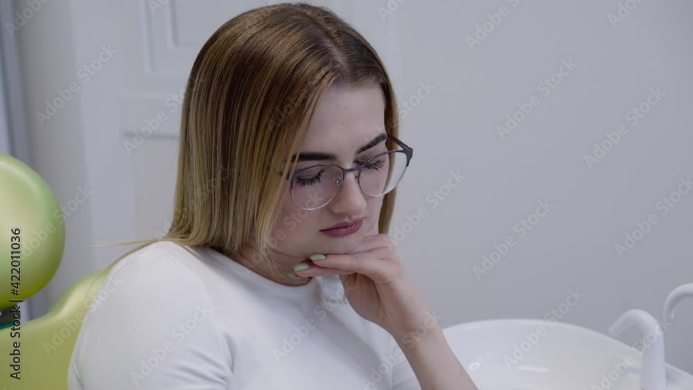 Sad female patient sits on dental chair with toothache and waits for theatment
