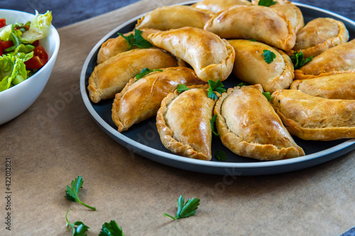 Traditional Latin American baked beef empanadas on a plate with a fresh salad sidedish. Gluten free savory pastries with meat stuffing or filing. Handmade typical dish in Spain or Argentina. Side view